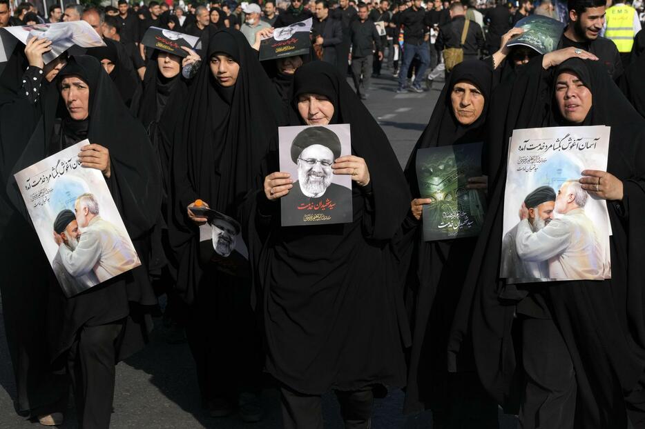 イランの故ライシ大統領のポスターを掲げ葬儀に参列する人々＝22日、テヘラン（AP＝共同）
