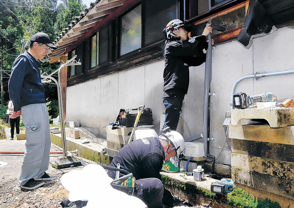前田さん（左）が見守る中、水道管工事を行う小松市の業者＝２９日午前１１時２０分、輪島市門前町浦上