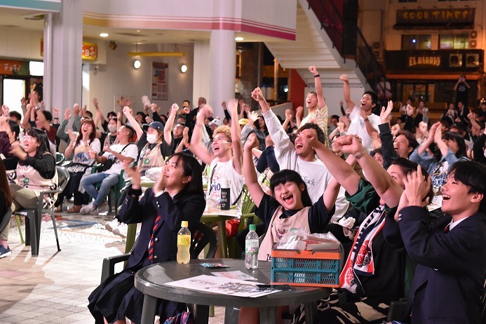 琉球ゴールデンキングスの選手のシュートが決まり、手を上げて喜ぶブースター＝13日、沖縄市のコザ・ミュージックタウン音市場