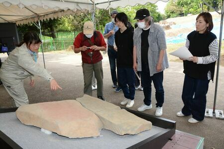 ３枚をつなぎ合わせた形で初めて展示された石棺墓の石ぶたに見入る見学者ら＝神埼市郡の吉野ケ里遺跡