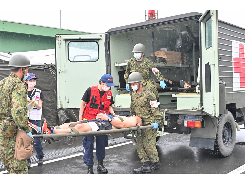 自衛隊救急車で搬送された患者役を、奄美駐屯地に設置されたSCUのテントへ運ぶ陸自隊員と県DMATの医師ら＝26日、鹿児島県奄美市名瀬の奄美駐屯地