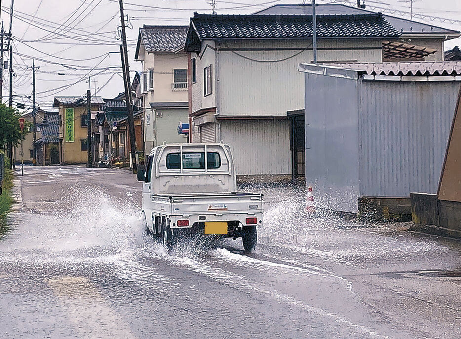 海水が流入した道路を水しぶきをあげて進む軽トラック＝２８日午前１１時半、七尾市石崎町