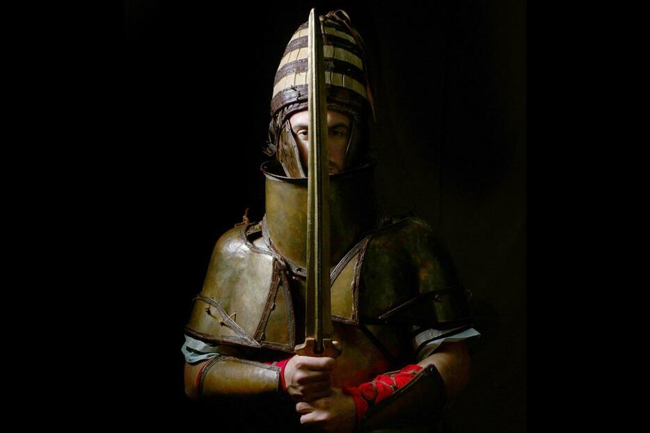 3500年前のデンドラの甲冑のレプリカを着用し、青銅器時代の剣のレプリカを持つギリシャ軍兵士。イノシシの牙から作られた兜は、ミケーネ時代の兵士の勇敢さと狩猟の腕前を表している。（ANDREAS FLOURIS AND MARIJA MARKOVIĆ）