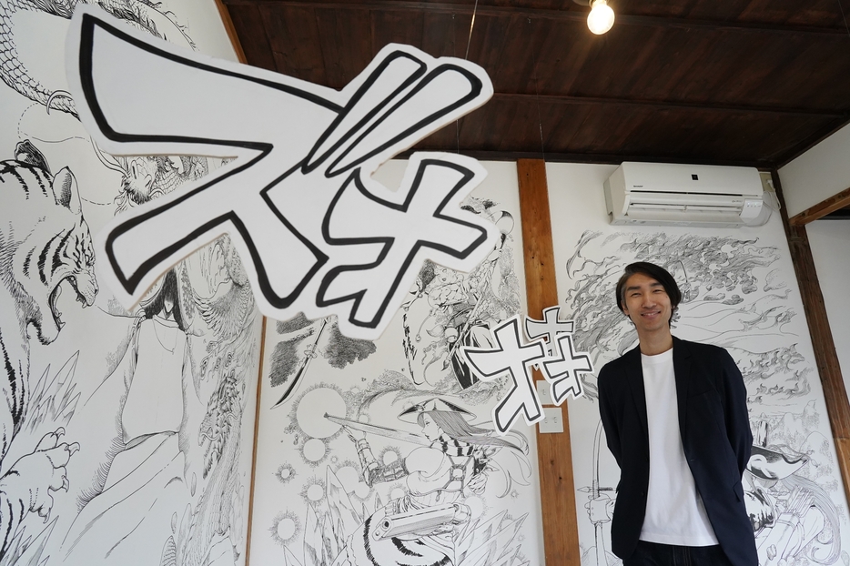 デザイン事務所内の壁面に描いたファンタジー世界と吉嶺さん＝兵庫県丹波篠山市西町で