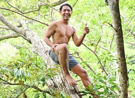 製作中のツリーハウスにある木の幹に腰をかけるキジーさん＝４月２２日、沖縄本島北部