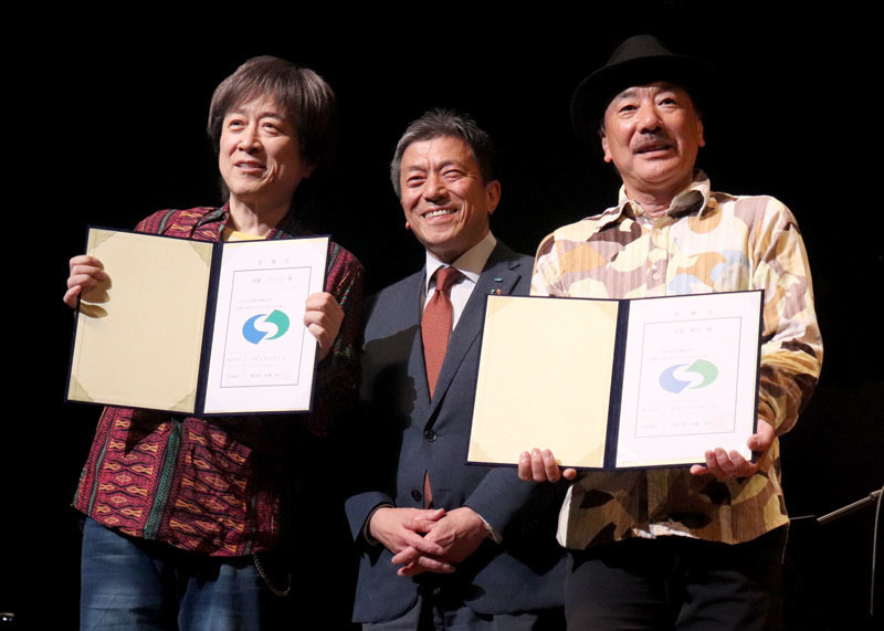 いちのせき大使の委嘱状を受け、コンサート中にステージで佐藤市長（中央）を囲む平賀さん（右）、高橋さん
