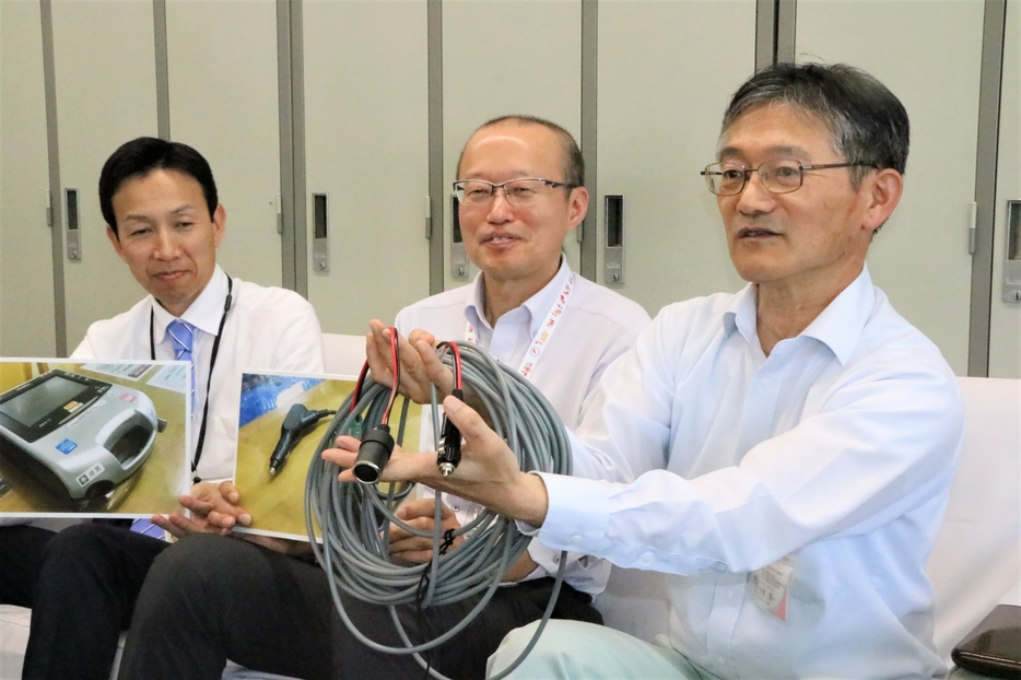 乗用車から人工呼吸器に給電できるケーブルについて説明する市職員有志=岡山県津山市で