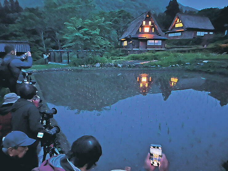 窓明かりがともされた家屋が水田に映る様子を収めようと集まったカメラマンたち=相倉合掌造り集落
