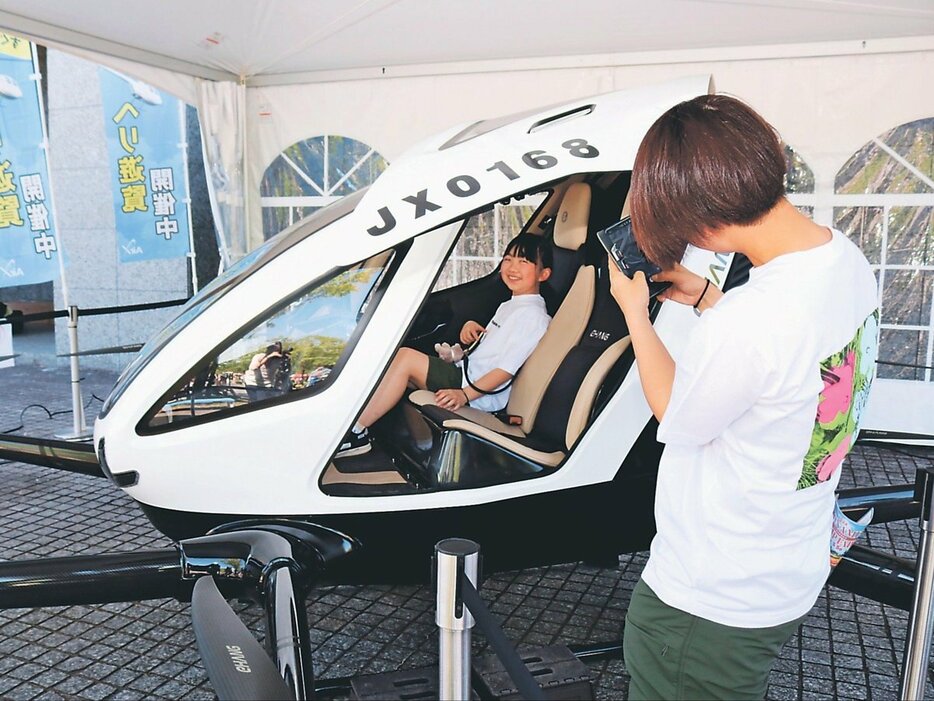 「空飛ぶクルマ」に搭乗して記念写真を撮ってもらう小学生＝砺波市美術館前