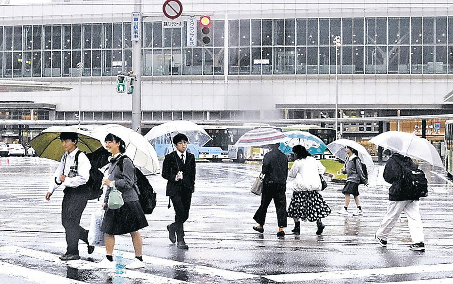 強い雨の中、傘を差して急ぐ人＝富山駅前