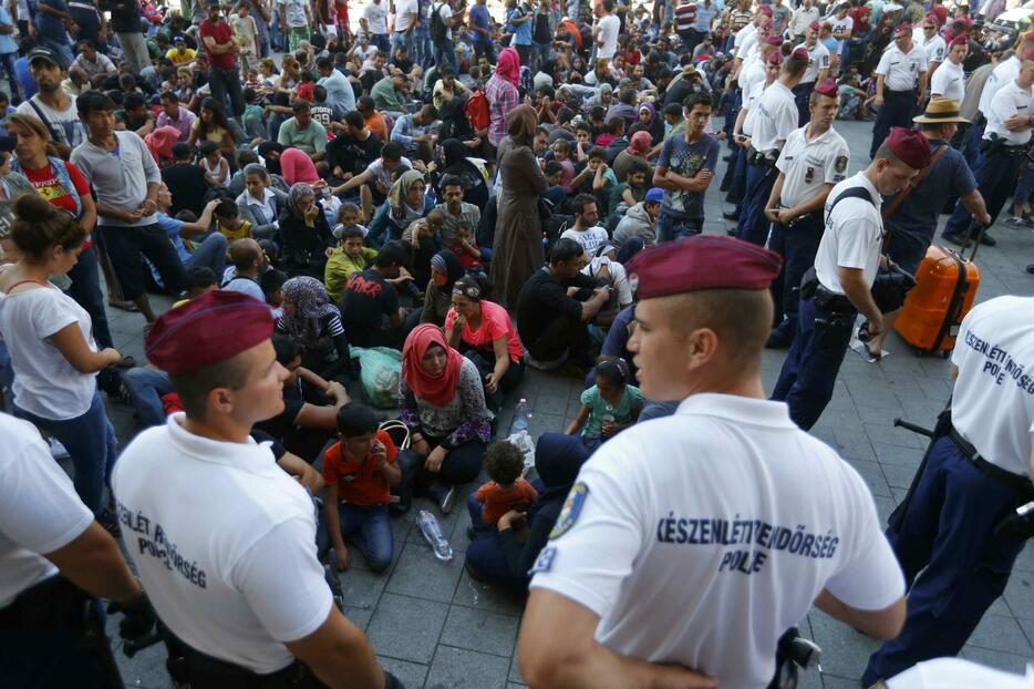 座り込む移民と見守るハンガリーの警官＝2015年9月1日（写真：ロイター/アフロ）