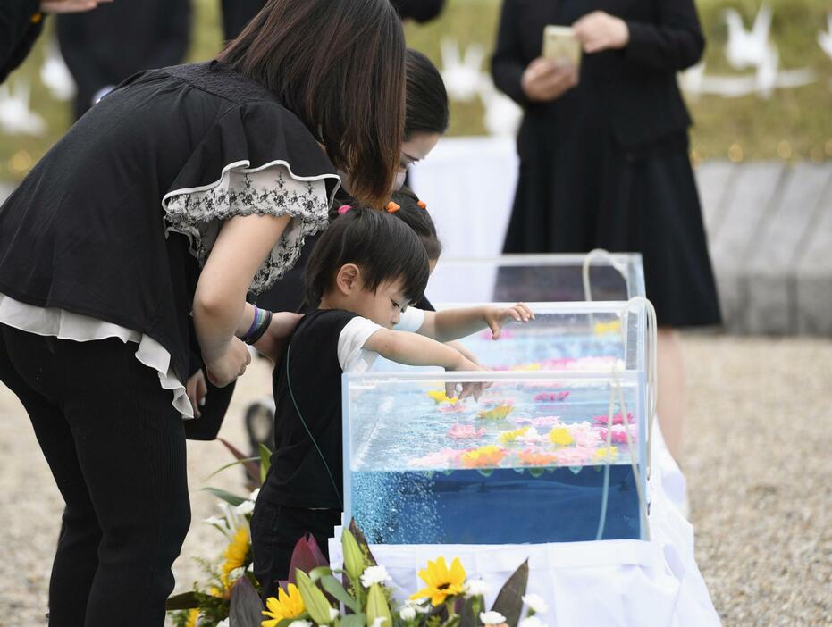 中華航空機墜落事故から30年となり、慰霊式で水槽に花を浮かべる参列者＝26日午後、愛知県春日井市