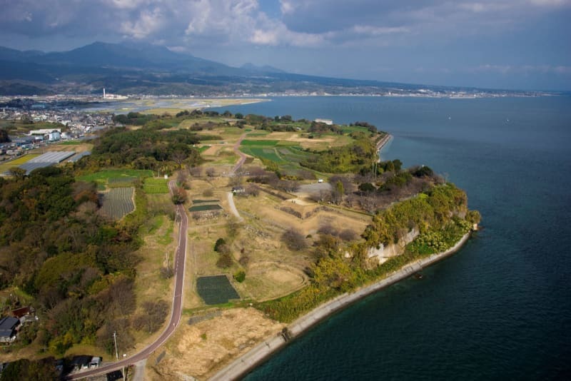 世界遺産の原城跡（中央の草地）＝長崎県南島原市（南島原市提供）、奥が雲仙・普賢岳