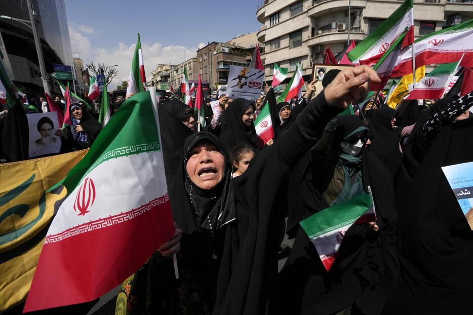 19日、テヘランで、イラン国旗を掲げながら反イスラエル集会に参加した人々（AP＝共同）