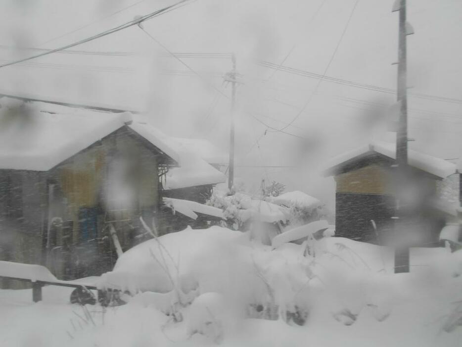 [写真]雪に覆われた飯山線沿線の住宅（列車から）