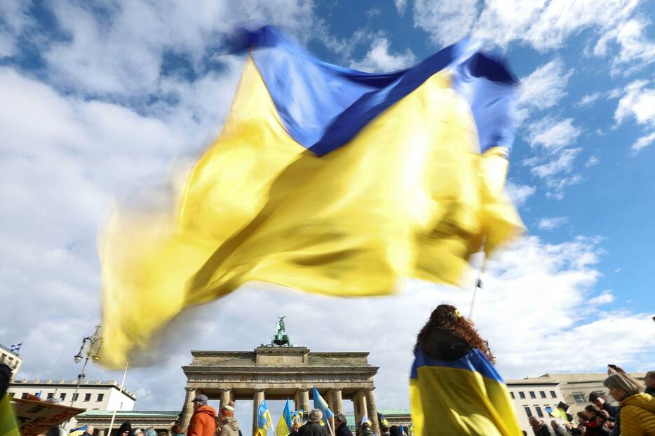 ブランデンブルク門の前で開かれたデモで振られるウクライナ国旗＝24日、ベルリン（ロイター＝共同）