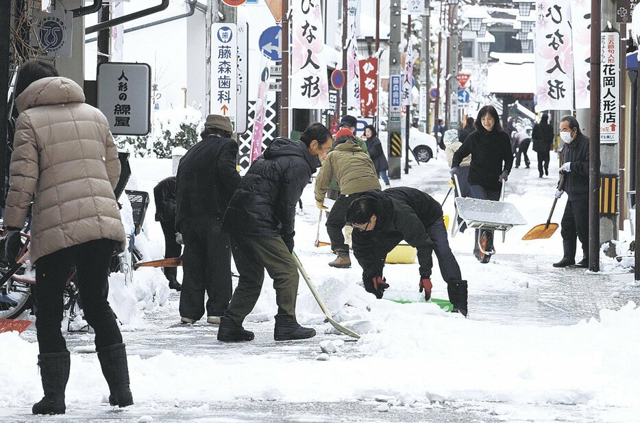 商店街の人たちが協力して固まった路面の雪を削り取り、運び出す（6日午前9時5分、松本市の高砂通り）