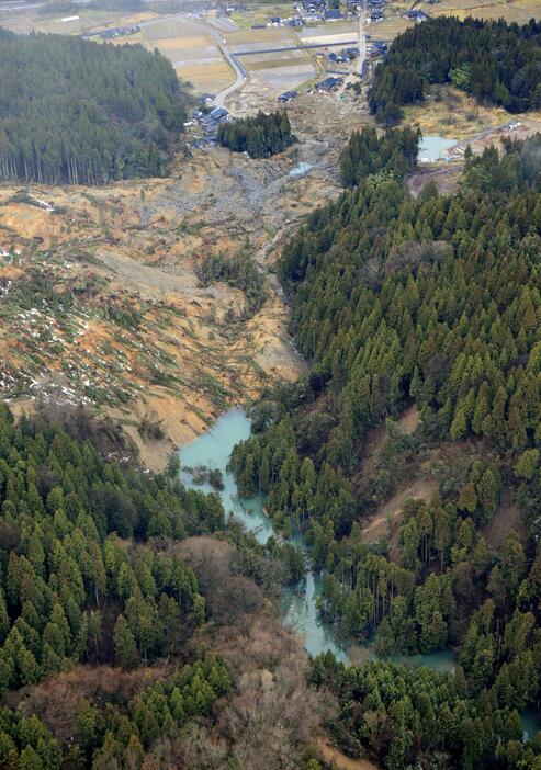 能登半島地震で崩れ、集落（奥）に迫る土砂。手前では川の流れがせき止められ「土砂ダム」が形成されていた＝7日午後3時57分、石川県輪島市（共同通信社ヘリから）