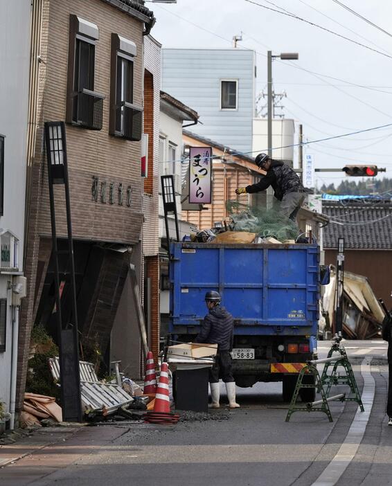 石川県珠洲市で緊急公費解体が始まり、傾いた住宅から家具などをトラックに積み込む業者ら＝26日午前