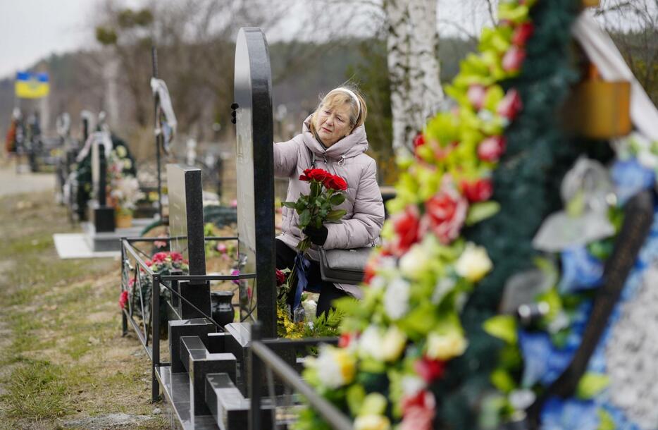 多数の市民が虐殺されたキーウ近郊ブチャにある墓地を訪れ、夫の遺影に手を伸ばすリュドミラ・キジロワさん（69）。夫は2022年3月、自宅庭でロシア軍に射殺された。「夫を亡くした痛みは今後も決して消えることはない」と悲しみに耐えるように話した＝23日（共同）