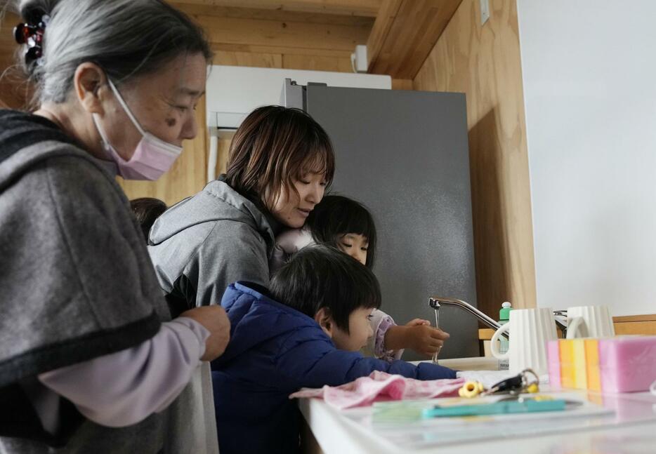 能登半島地震の被災者向けに建設された応急仮設住宅に入った大下澄子さん（左端）の部屋で蛇口からの水に触れるひ孫ら。歓声を上げていた＝3日午後、石川県輪島市