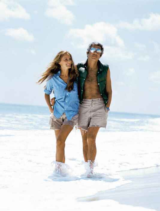 リッキー＆ラルフ・ローレン夫妻。1977年、モントークにて RICKY AND RALPH LAUREN ON THE BEACH IN THE HAMPTONS, NY. (LES GOLDBERG, 1977)