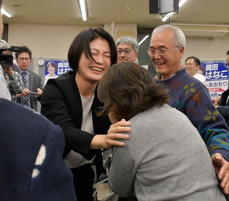 当選確実の報を受け支援者と抱き合う岡田さん＝27日午後11時3分