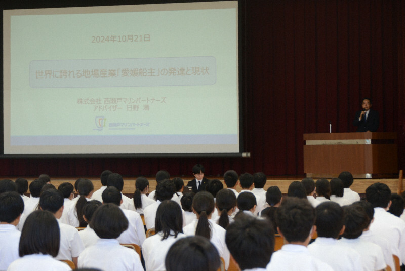 造船や海運業が盛んな愛媛県今治市の地場産業を伝える出前授業で、登壇した日野さん（右奥）の話を聞く生徒ら＝同市立日吉中学校で2024年10月21日午後1時34分、鶴見泰寿撮影