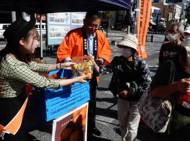 刀根早生が2個入った袋が県民や観光客らに無料配布された=25日、奈良市三条本町のJR奈良駅前広場