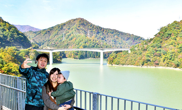 紅葉が進むダム湖を背景に写真を撮る来場者＝長井市・長井ダム周辺