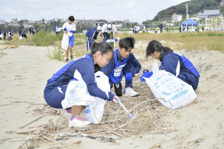 海岸に落ちているごみを拾い集める高校生