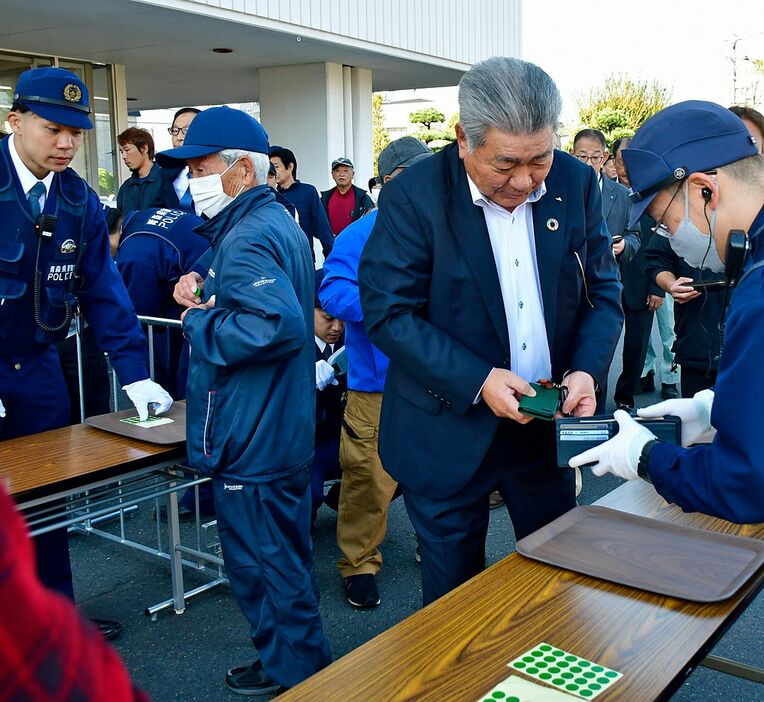 警察による手荷物チェックを受ける聴衆＝22日午前、三沢市役所駐車場