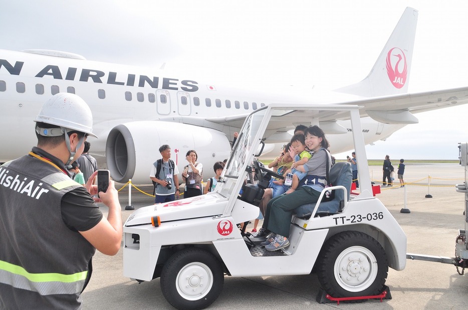 手荷物をけん引する車両に乗り、飛行機をバックに写真撮影する参加者（山口宇部空港で）