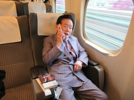 新幹線の車内で携帯電話で通話する野崎幸助氏。スマホも所持していたが、愛用していたのはもぱらガラケーだった（撮影：吉田 隆）