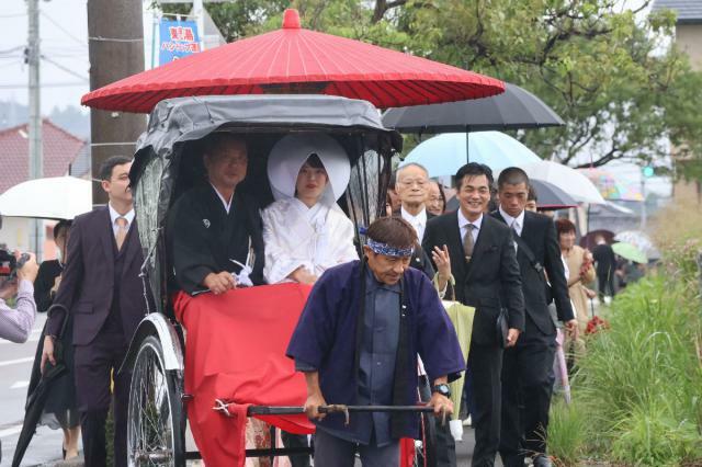 人力車に乗った花嫁とその父親に沿道から祝福の言葉がかけられた花嫁行列