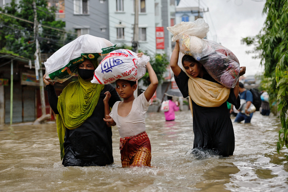 　南アジアでは豪雨の頻度が高まって国境をまたぐ洪水を引き起こしており、専門家は、地域各国による密接な協力の必要性を指摘している。写真は洪水の中で荷物を運ぶ人々。８月、バングラデシュ・フェニで撮影（２０２４年　ロイター/Mohammad Ponir Hossain）