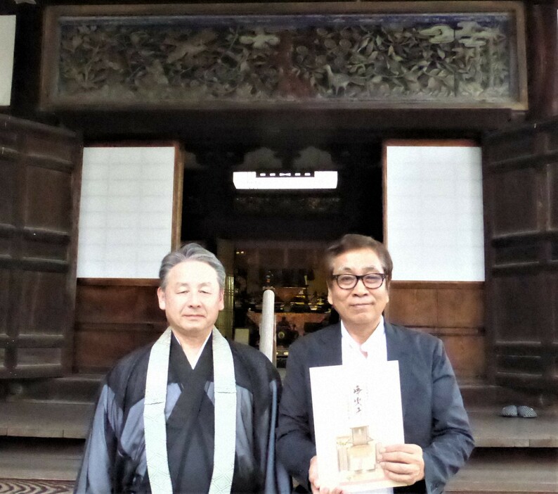 刊行した「浄楽寺総合調査報告書」を手に浄楽寺の本堂前に立つ檀家惣代の大西甚吾さん（右）と近藤正暢住職。本堂上部に旧多武峰妙楽寺から転用された大欄間がみえる＝奈良県橿原市中町で2024年10月7日、皆木成実撮影