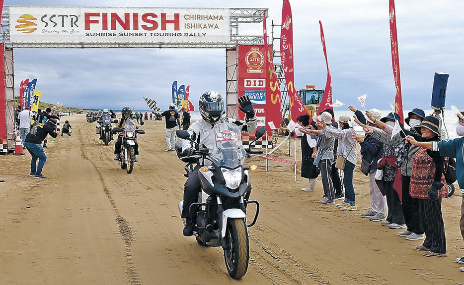 住民の歓迎を受けながらゴールする全国のライダー＝羽咋市千里浜海岸