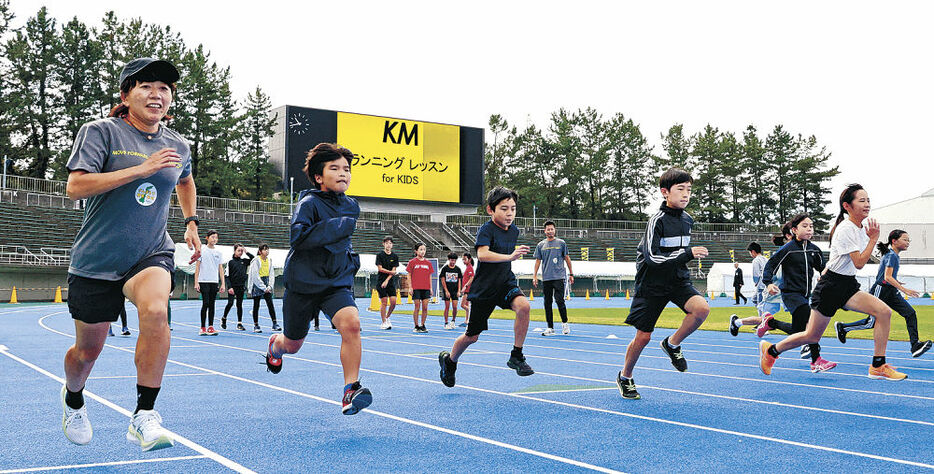 野口さん（左）と一緒にレッスンを楽しむ児童＝２６日午前１０時４０分、金沢市の石川県陸上競技場