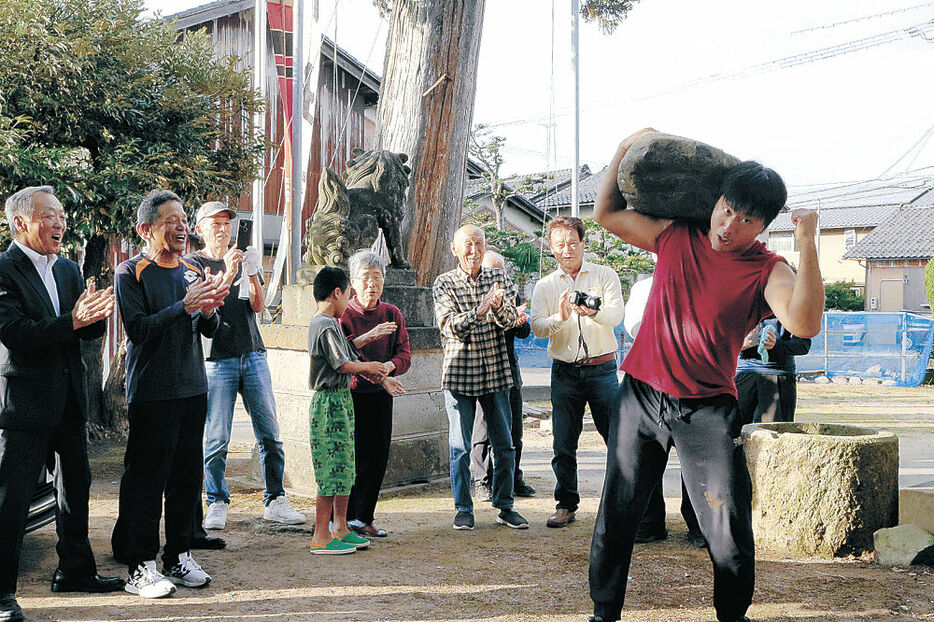 石を持ち上げガッツポーズを見せる西野さん（右）＝津幡町太田の八幡神社