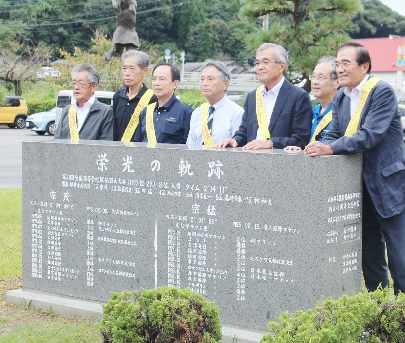 移設された記念碑の前で都大路出場時の仲間と記念撮影する宗兄弟。右端が茂さん、右から3人目が猛さん