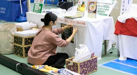 産業まつりで自社の取り組み紹介のポップを展示する担当者＝２４日、那覇市の県立武道館