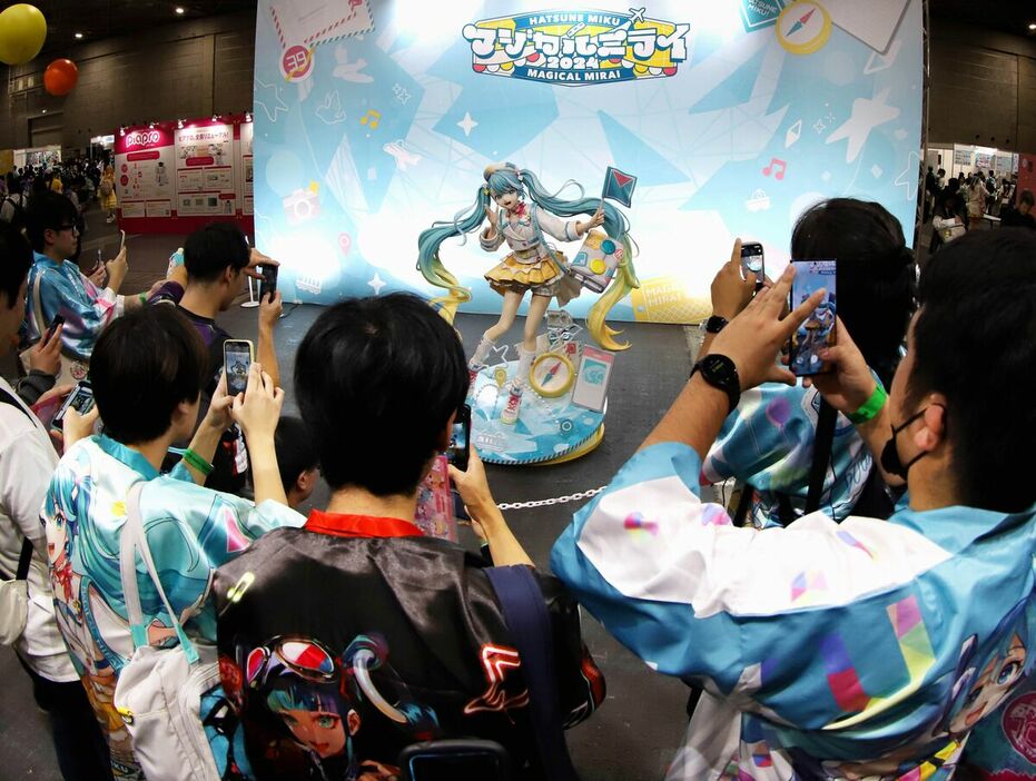 イベントテーマ「ファンファントリップ」をイメージした衣装の初音ミクの等身大立像にスマホのカメラを向けるミクファン