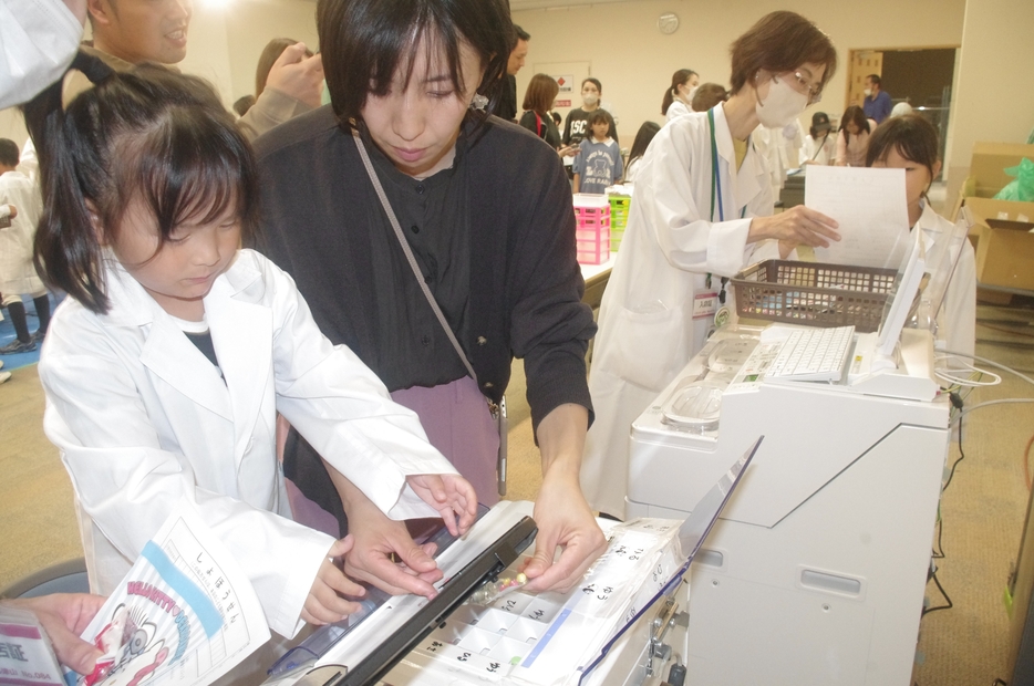 白衣に身を包み、調剤体験をする子どもたち=岡山県津山市で