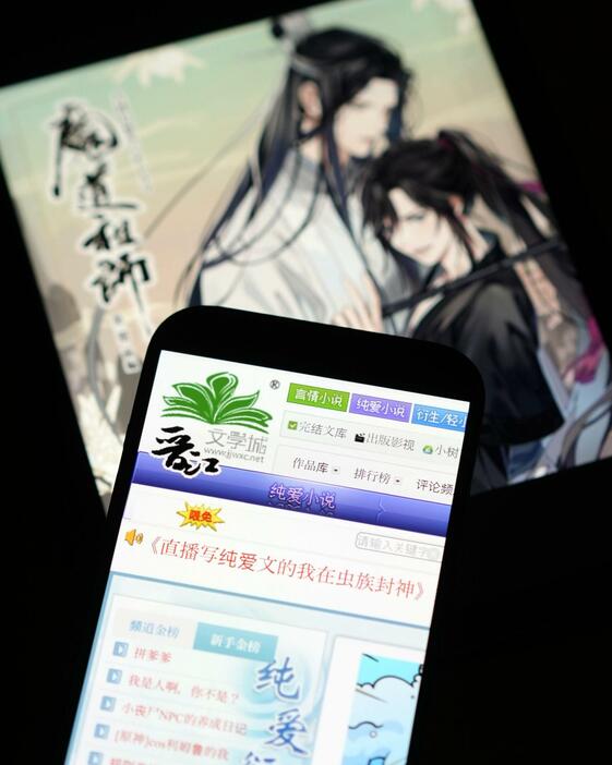 スマートフォンの画面に表示された文学投稿サイト「晋江文学城」。奥はアニメ化された墨香銅臭さんの作品（共同）