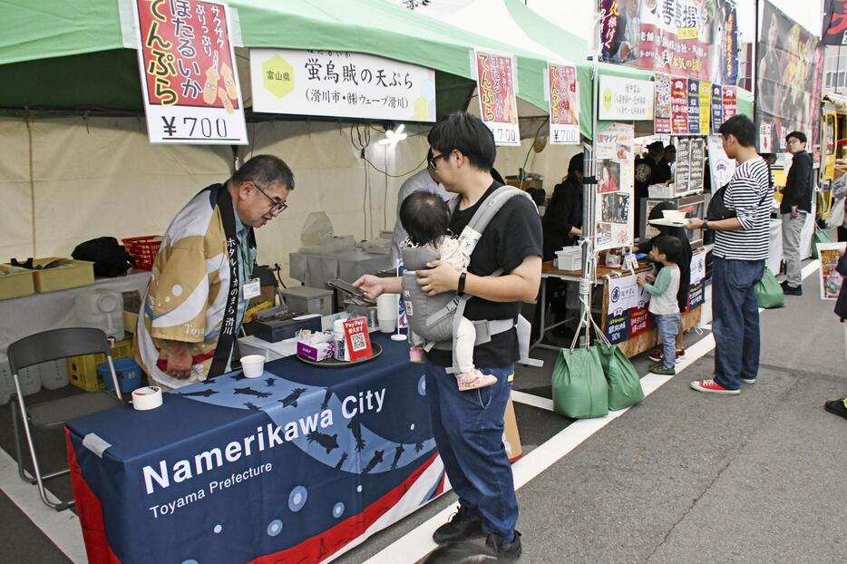 富山県滑川市のブースで名産品を購入する来場者＝5日午後、石川県加賀市