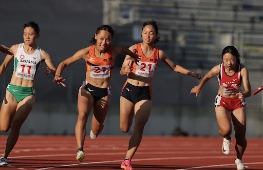 成年少年女子共通400メートルリレー決勝　3走•渡辺（21右）からアンカーの小針にバトンをつなぐ。大会新記録で優勝した＝SAGAスタジアム