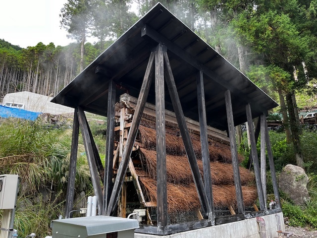 建物の裏手からもくもくと煙をたてながら湧き出る源泉と、お湯の冷却装置「湯雨竹」。