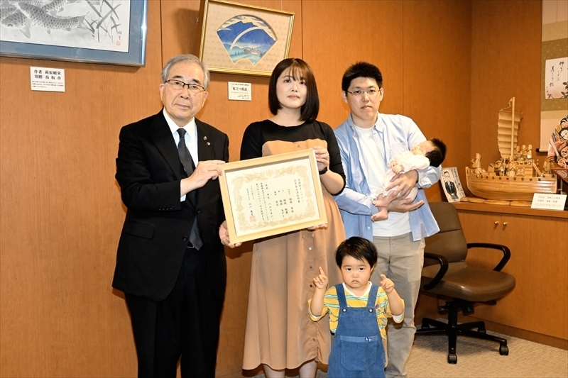 品川市長から証明書を受け取るあずささん（中央）。右が芽依ちゃんを抱える裕貴さん、手前が稜久ちゃん