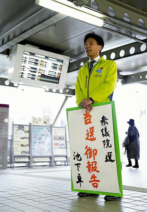 「当選御報告」と書いたポスターを手にあいさつする池下さん（大阪府高槻市で）